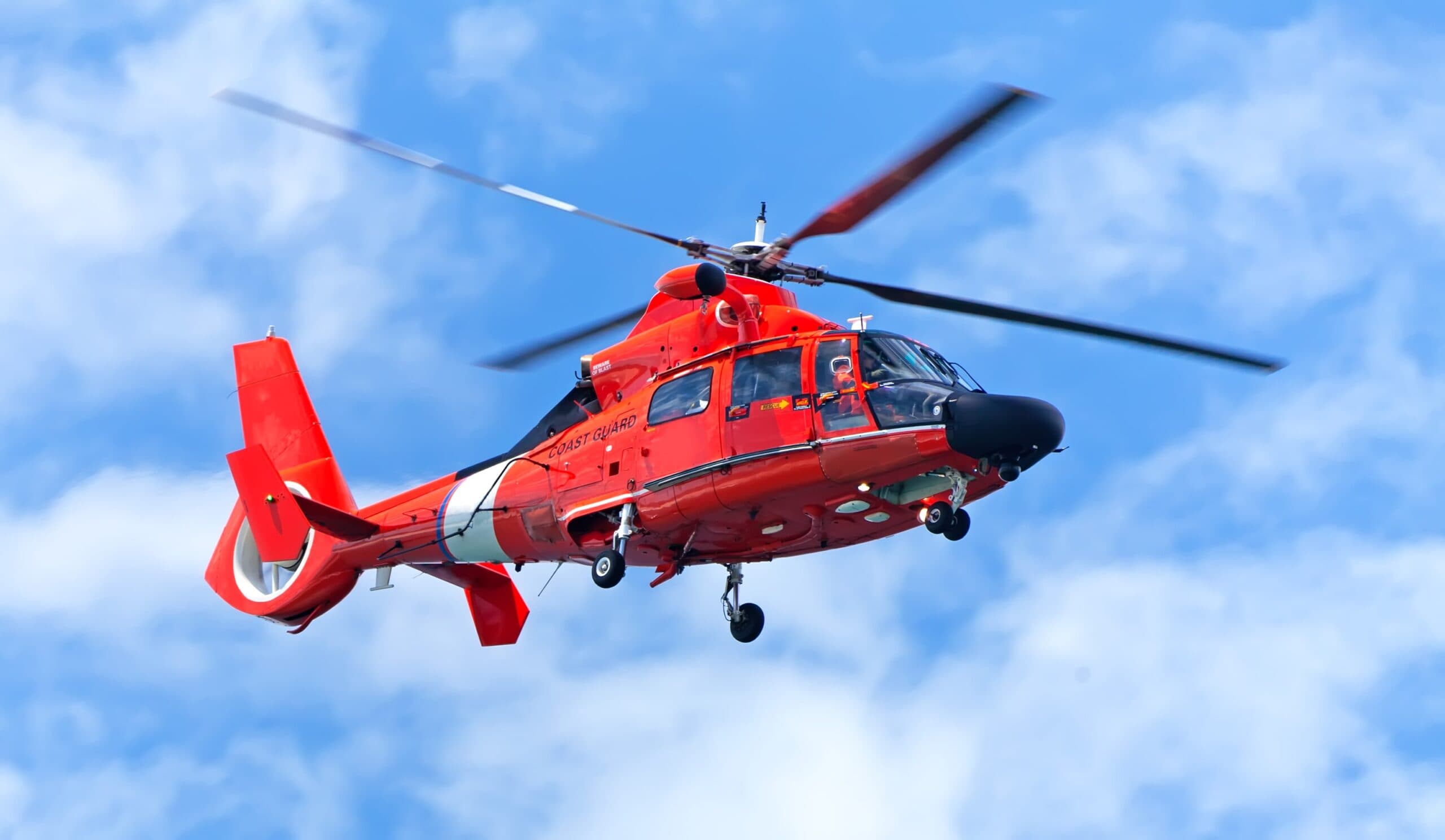 A red coast guard helicopter flying in the sky.