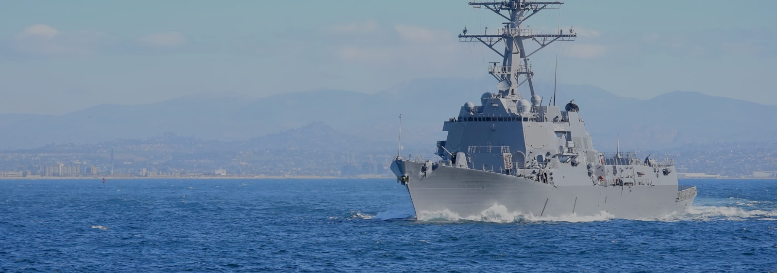 A navy ship in the ocean with mountains in the background.