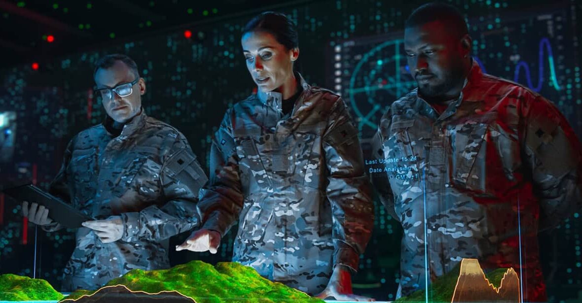 Three uniformed individuals analyze a 3D topographic map in a high-tech room with digital displays and data visuals.