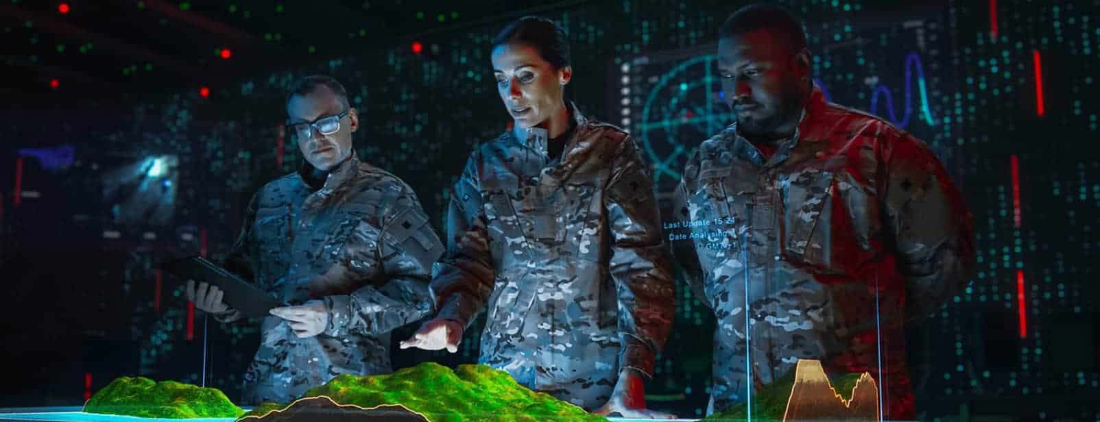 Three uniformed individuals analyze a 3D topographic map in a high-tech room with digital displays and data visuals.